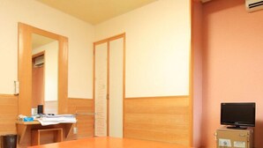 Une pièce avec une table en bois, un téléviseur posé sur un meuble, un bureau avec un ordinateur et un miroir.