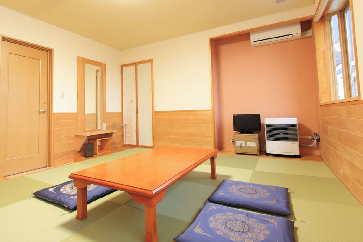 Una habitación con una mesa de madera, esteras de tatami, un televisor y un equipo de aire acondicionado.