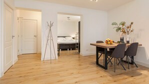 A modern apartment with a wooden floor, a dining area with a table and chairs, a bed, and a hallway leading to another room.