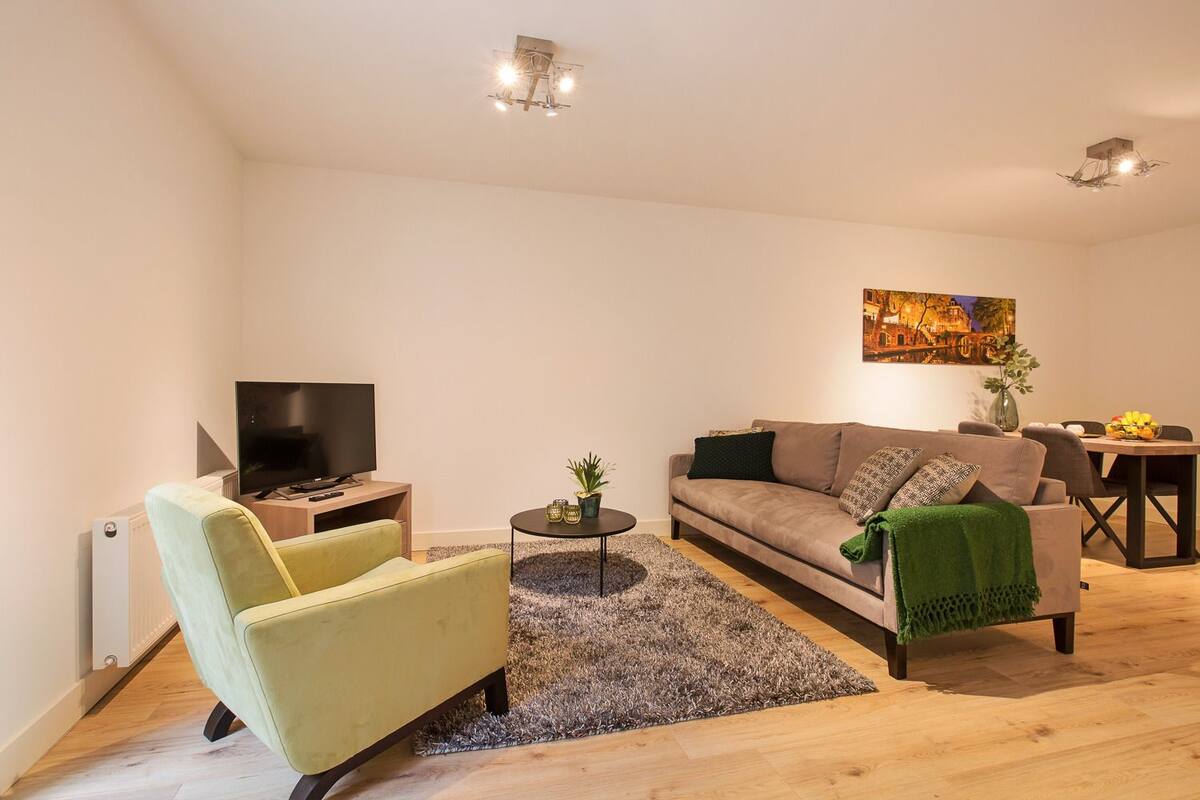 A modern living room with a sofa, a television, a small side table, and a dining area with a table and chairs.