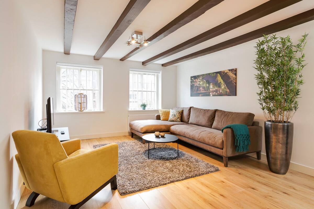 A living room with a sofa, a yellow armchair, a coffee table, and a large potted plant.