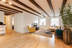 A modern living room with wooden flooring, a sofa, a yellow armchair, a TV, and a large potted plant. - Canal Garden Apartment (Utrecht)