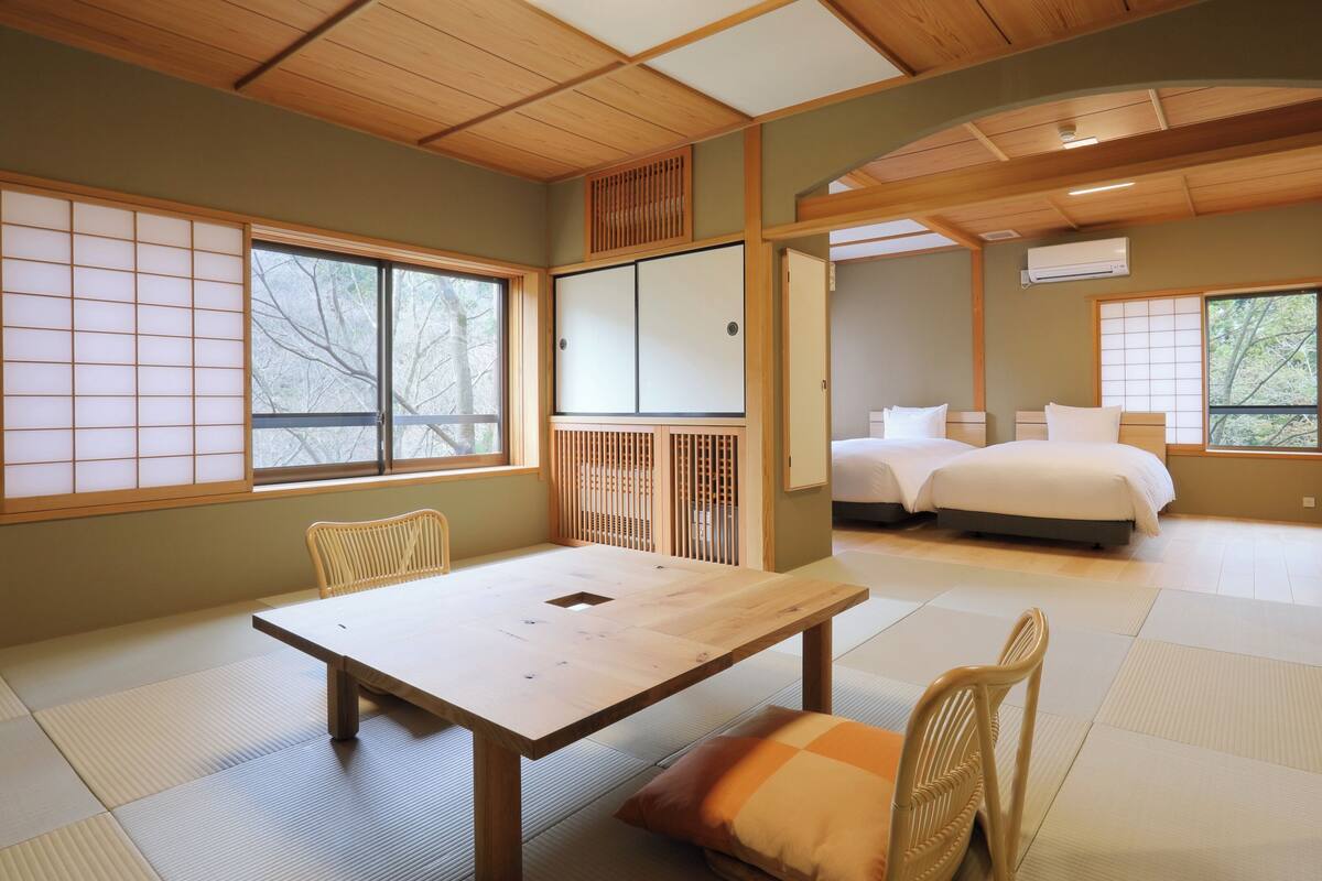 Een traditionele Japanse kamer met tatami vloerbedekking, een houten tafel, stoelen, een bed en schuifdeuren.