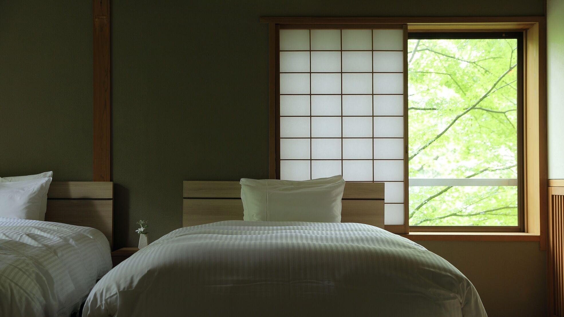 A room with two beds, a large window with a view of trees, and a traditional sliding door.