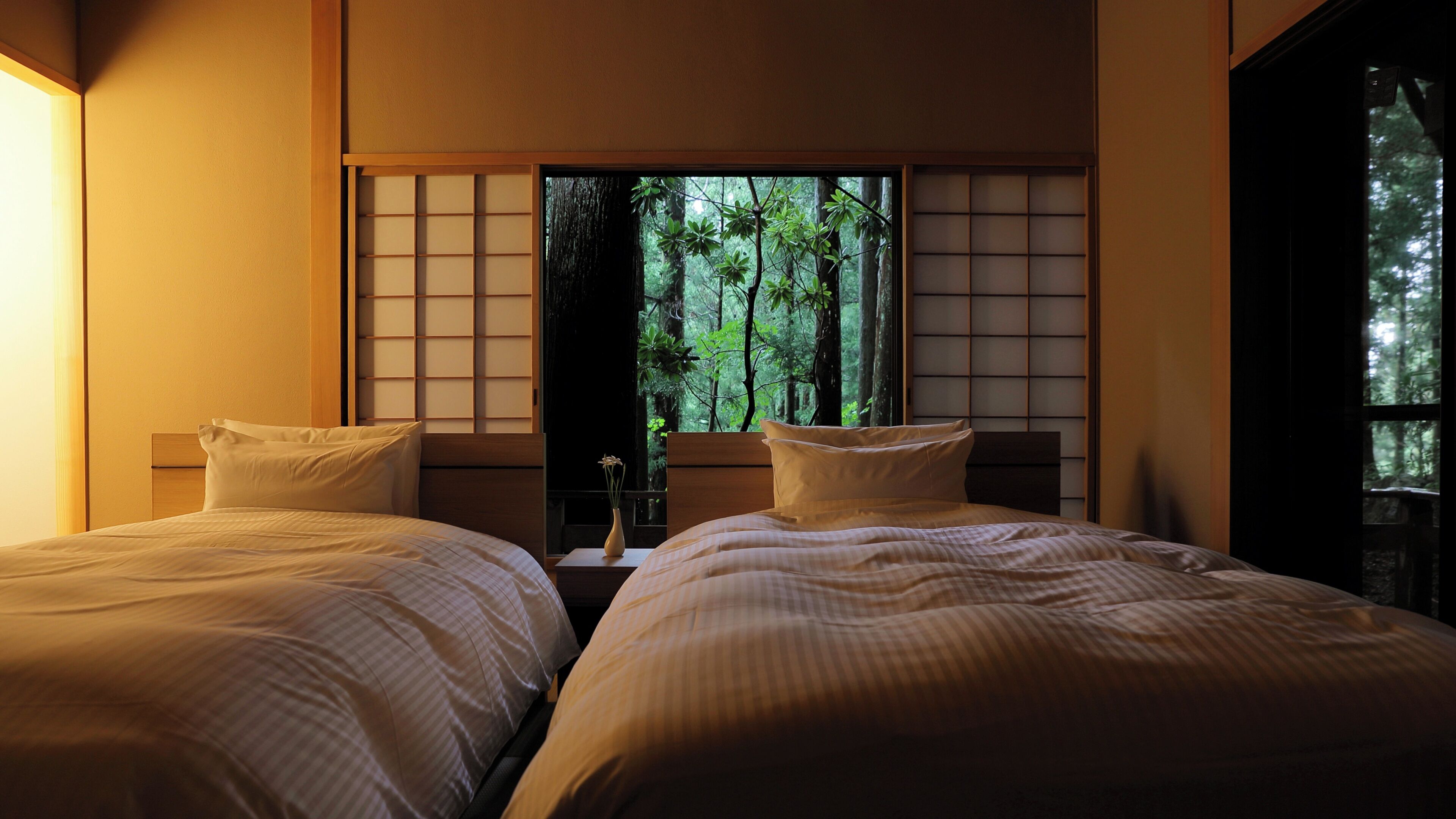 A room with two beds, a view of a forest through a window, and a traditional Japanese sliding door.