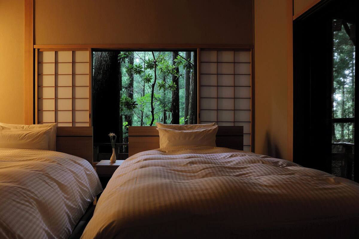 Een kamer met twee bedden, uitzicht op een bos door een raam en een traditionele Japanse glijdeur.