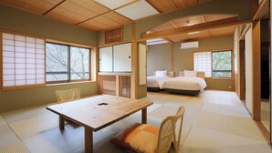 Una habitación japonesa tradicional con suelo de tatami, una mesa de madera, sillas, una cama y puertas correderas.