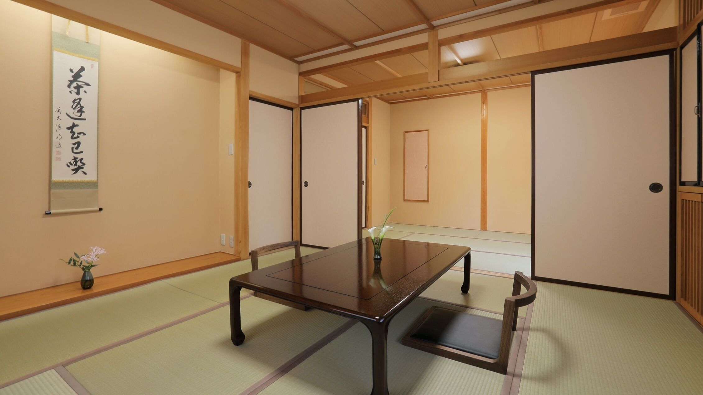 A traditional Japanese room with tatami flooring, a low table, sliding doors, and a calligraphy scroll.