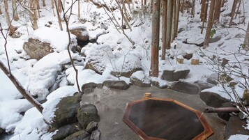 Una fuente termal de piedra rodeada de rocas y árboles cubiertos de nieve.