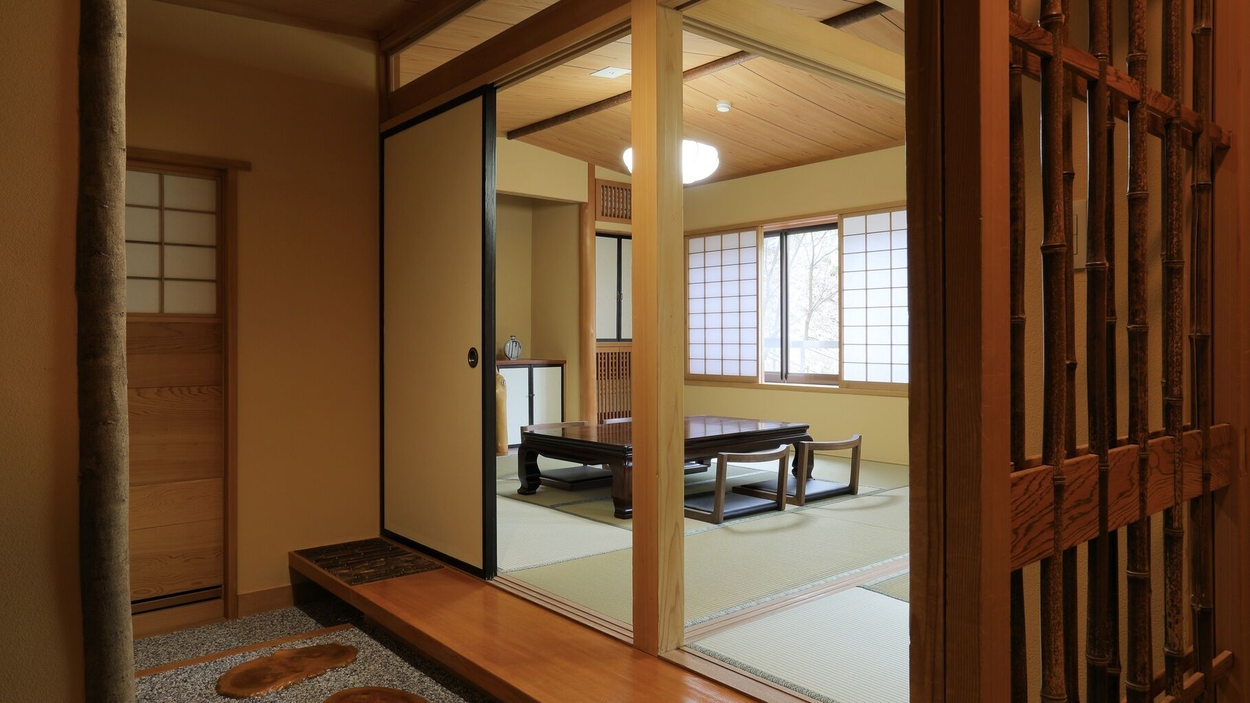A traditional Japanese room with tatami flooring, a sliding door, a wooden table, and a view through the door.