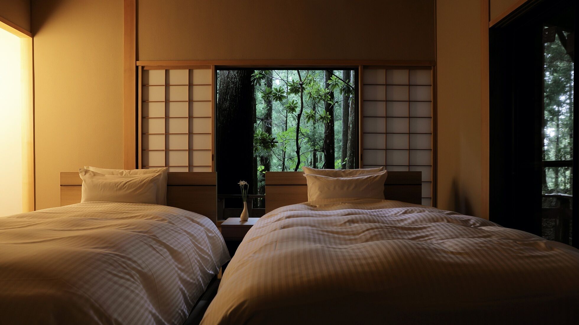 A room with two beds, a window with a view of trees, and a traditional sliding door.