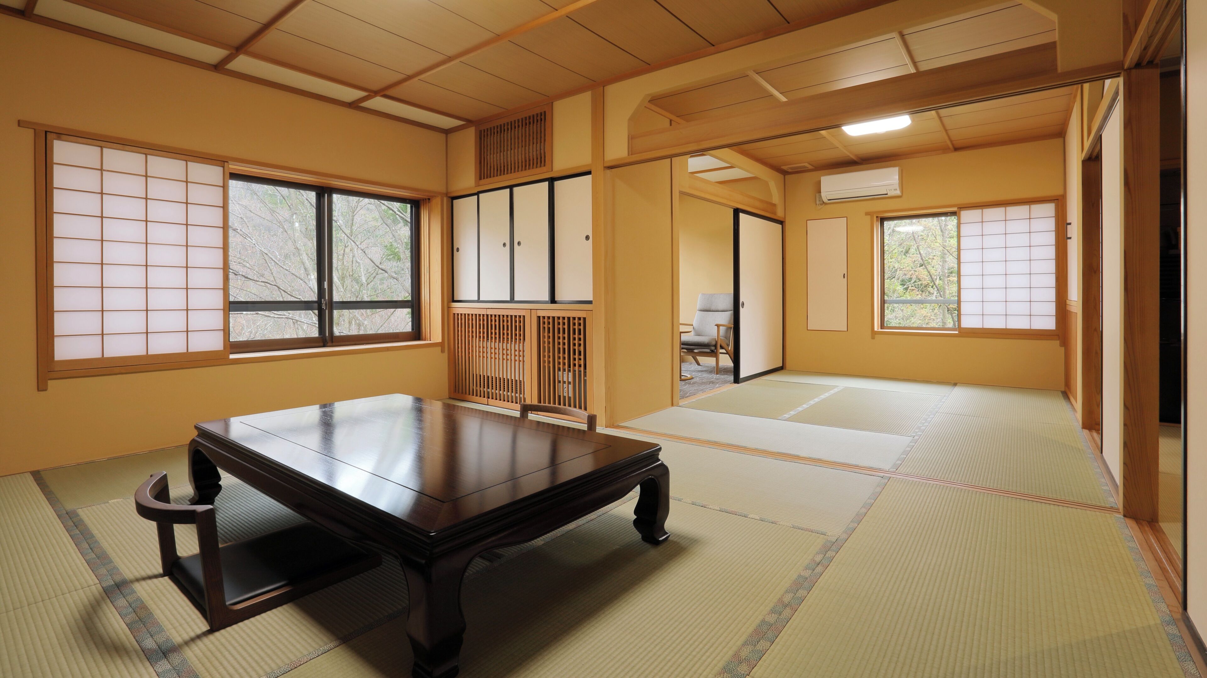 A traditional Japanese room with tatami flooring, a low wooden table, sliding doors, and a view through the windows.
