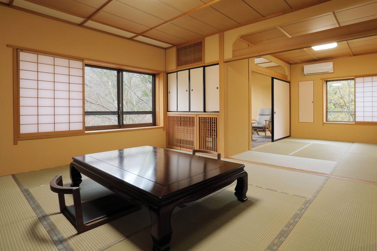 Een traditionele Japanse kamer met tatami vloerbedekking, een lage houten tafel, schuifdeuren en uitzicht door de ramen.