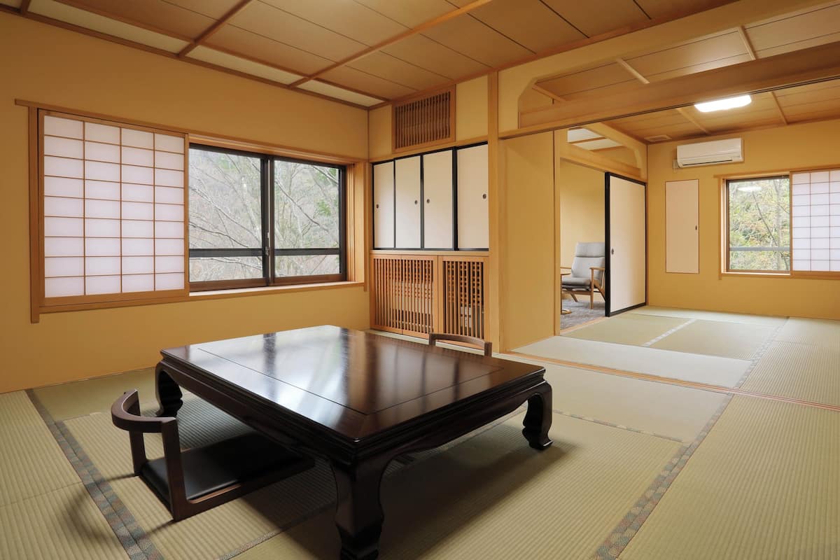 A traditional Japanese room with tatami flooring, a low wooden table, sliding doors, and a view through the windows.