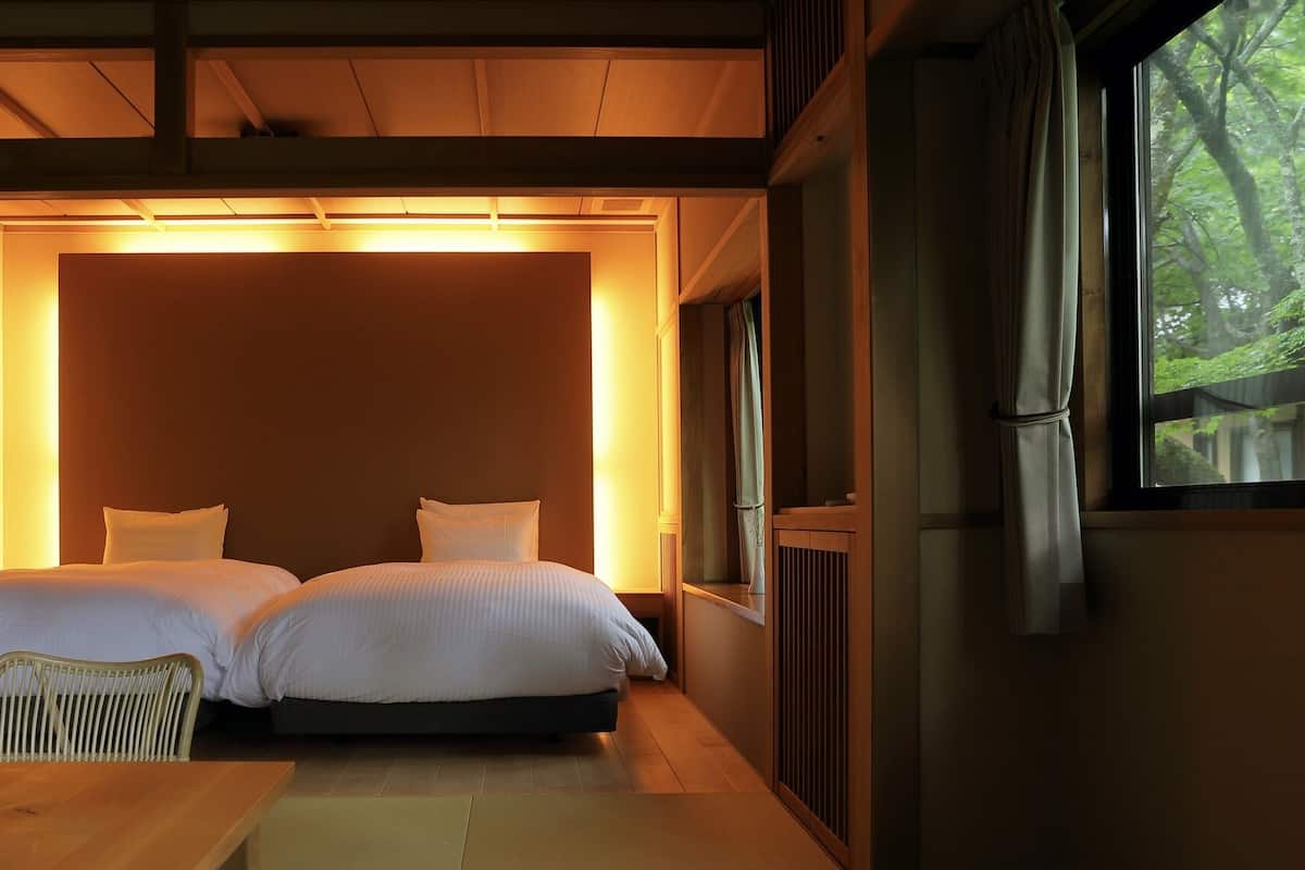 Een kamer met twee bedden, een houten tafel en een raam met uitzicht op bomen.