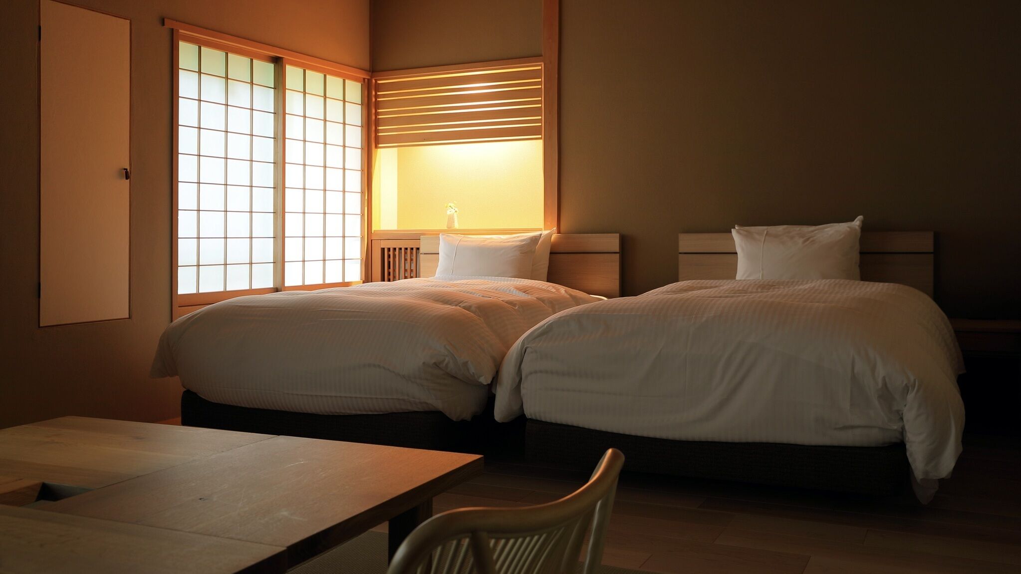 A room with two beds, a table, and a chair.