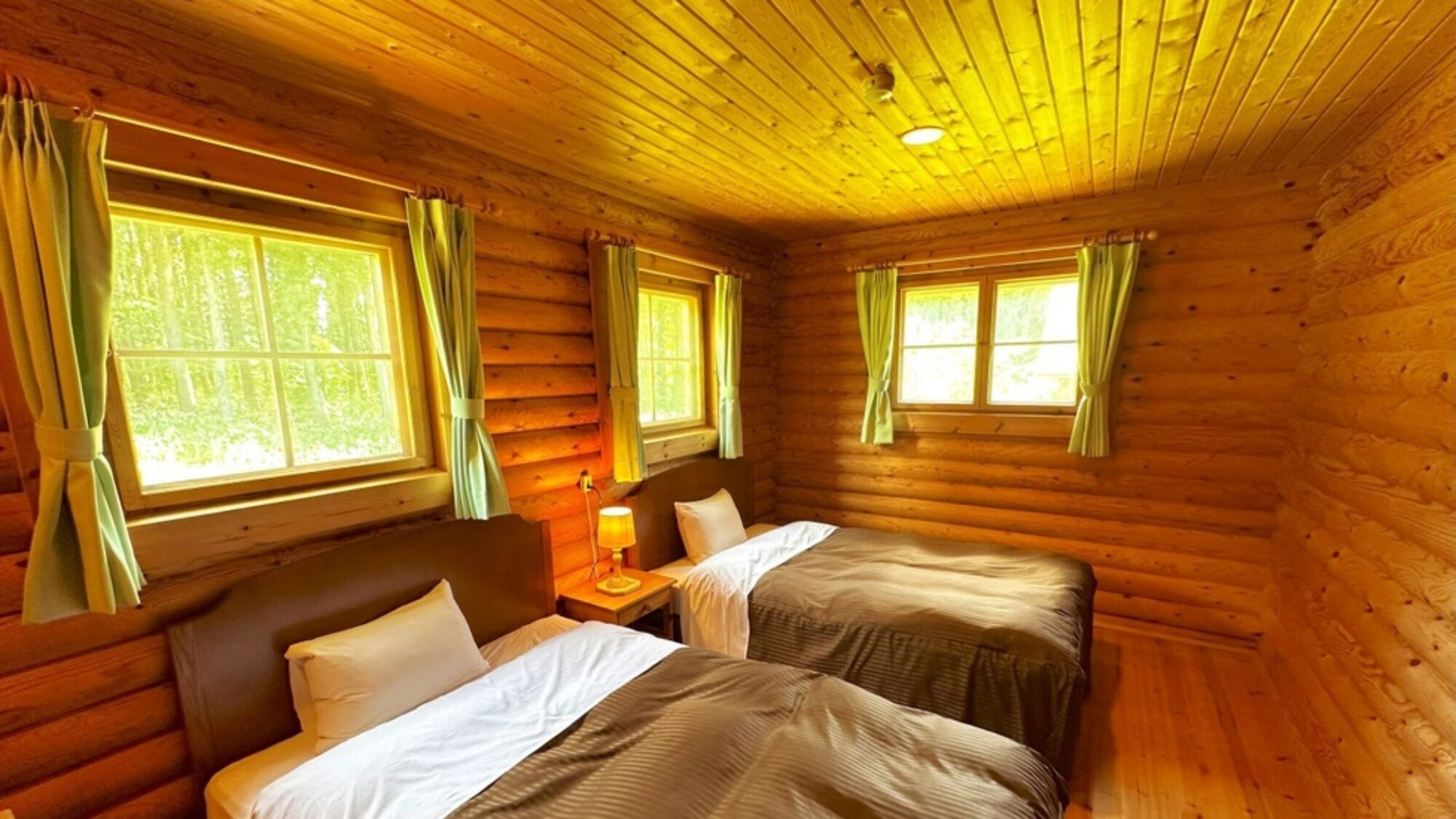 Une chambre de style rustique, avec deux lits, des murs en bois et de grandes fenêtres dotées de rideaux.