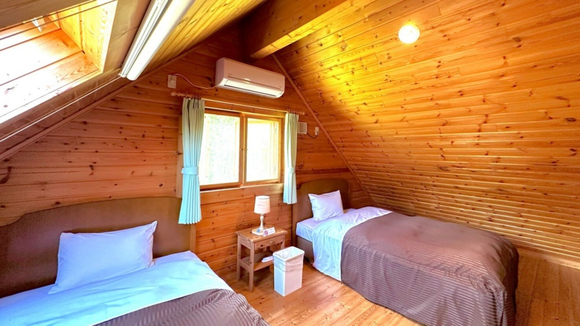 Une chambre confortable située sous les toits, avec deux lits, une petite table et un appareil de climatisation.