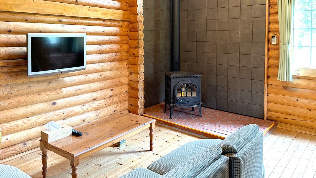 A log cabin interior with a television, a fireplace, a sofa, and a wooden table.