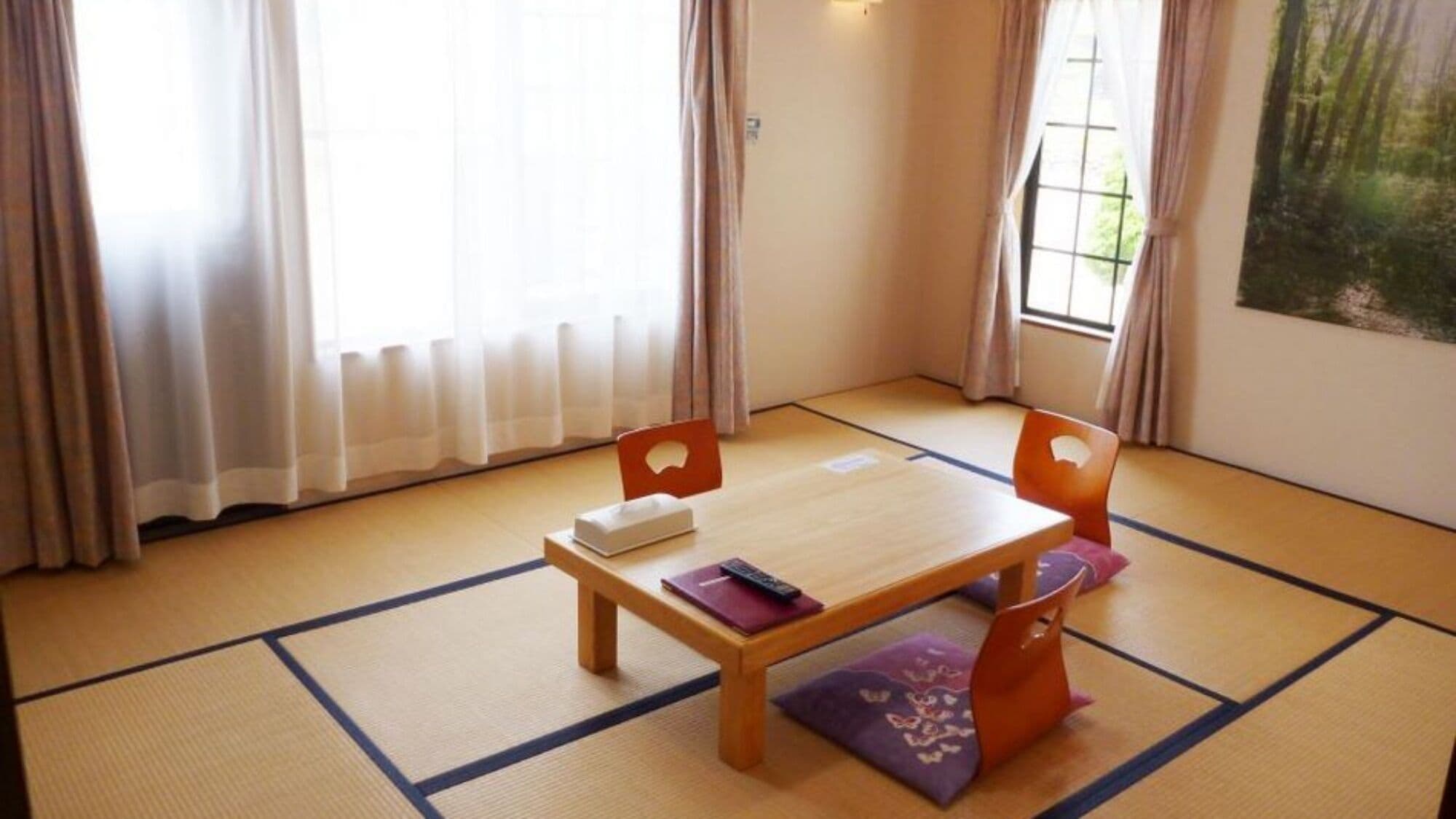 Une pièce avec un sol recouvert de tatamis, une table en bois, deux chaises, un lit et une fenêtre avec des rideaux.