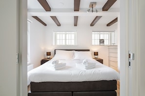 A modern bedroom with a large bed, two bedside tables with lamps, and a window with a decorative frame.
