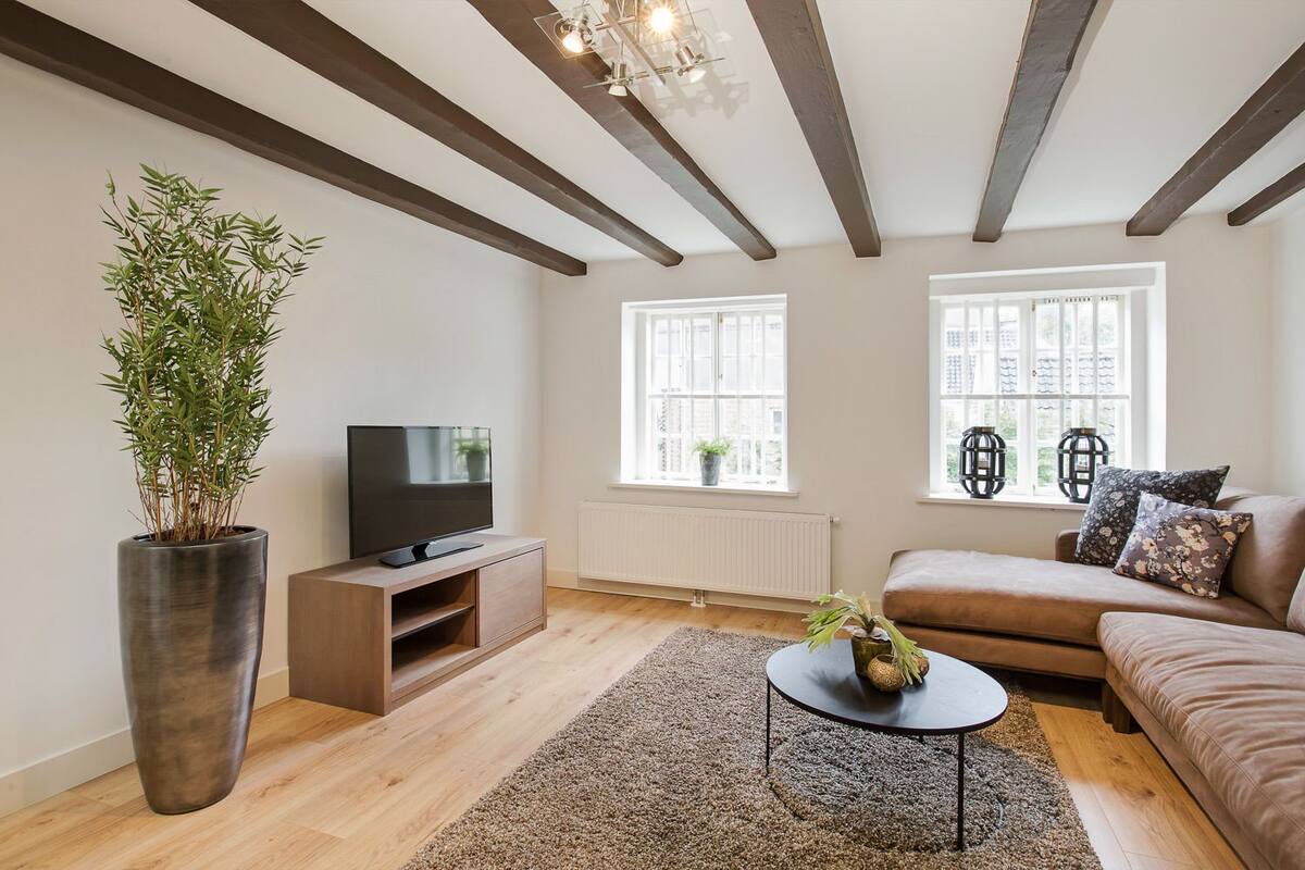 Uma sala de estar moderna com uma televisão grande, um sofá, uma mesa de centro e um vaso com planta.