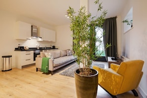 A modern apartment with a kitchen, living area, and a large potted bamboo plant.