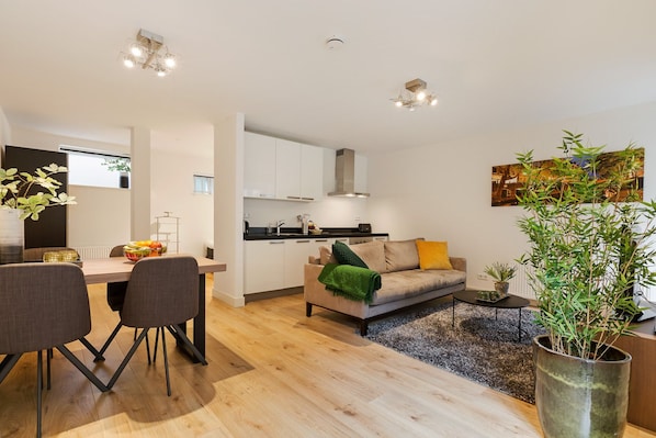 A modern apartment with a dining area, kitchen, living room, and a large potted plant.