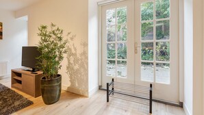 A modern living room with a television, a large potted bamboo plant, and a sliding glass door leading to a garden. - Canal Garden Apartment 11 (Utrecht)