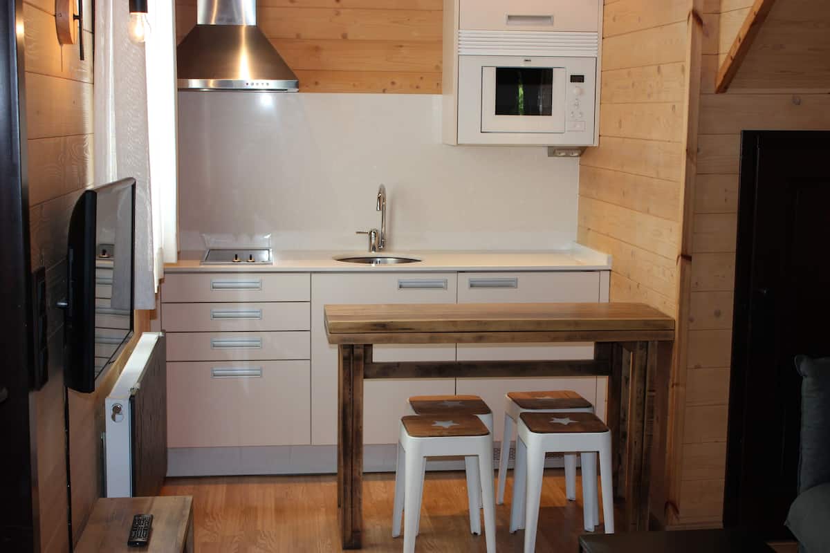 Una cocina compacta con una mesa de madera y taburetes, un microondas integrado y una campana extractora de acero inoxidable.