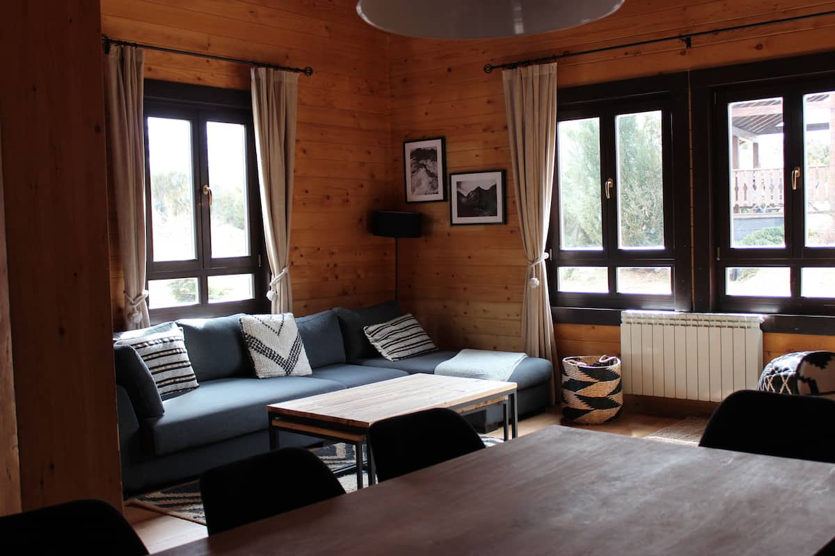 Un interior acogedor de cabaña con paredes y mobiliario de madera, un sofá, una mesa y una silla.