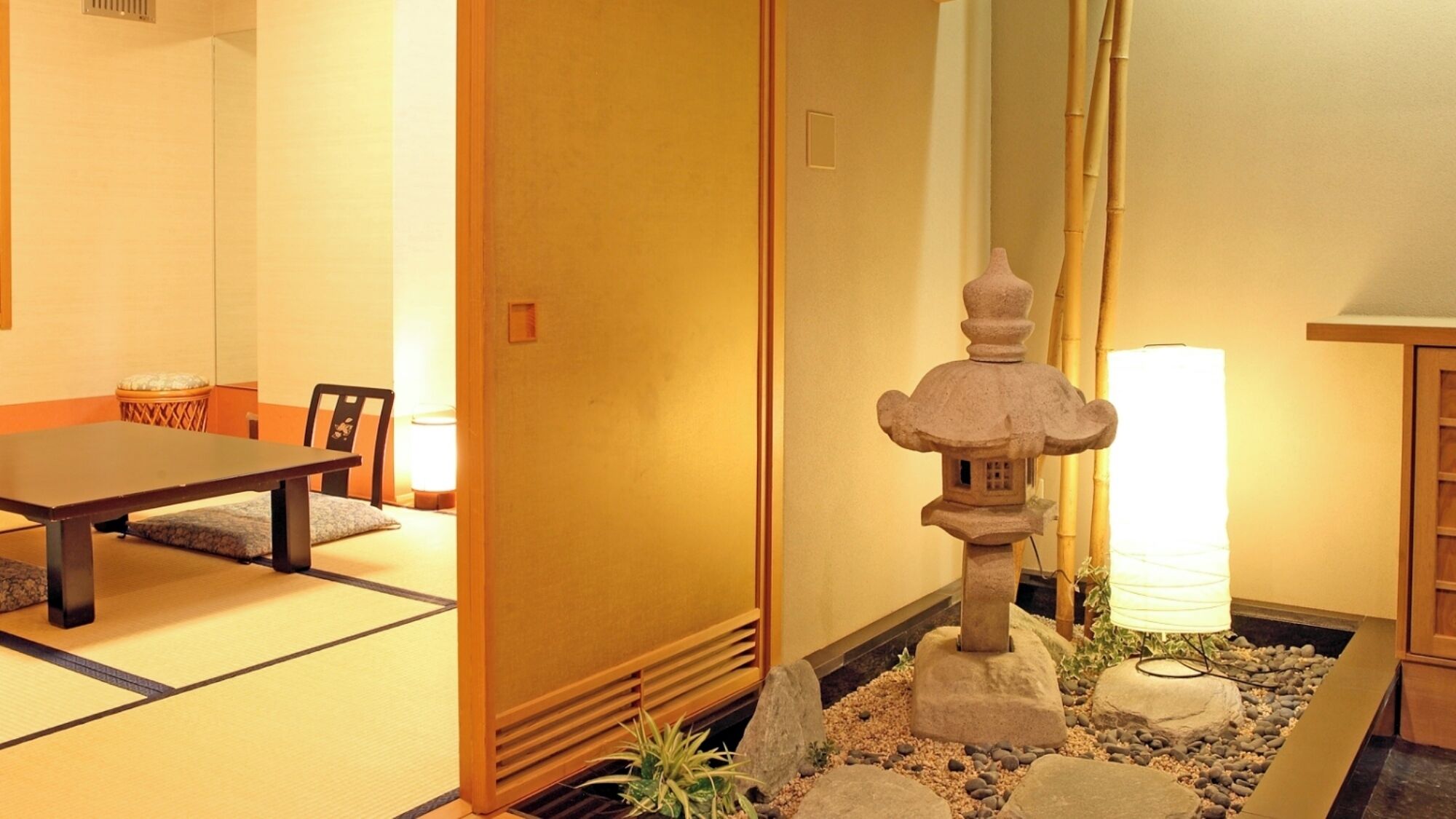 A traditional Japanese room with tatami flooring, a low table, chairs, a shoji screen, a stone lantern, and a small rock garden.