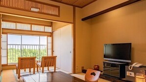 Een traditionele Japanse kamer met tatami vloeren, een lage houten tafel, stoelen, een televisie en een schuifdeur naar een balkon.