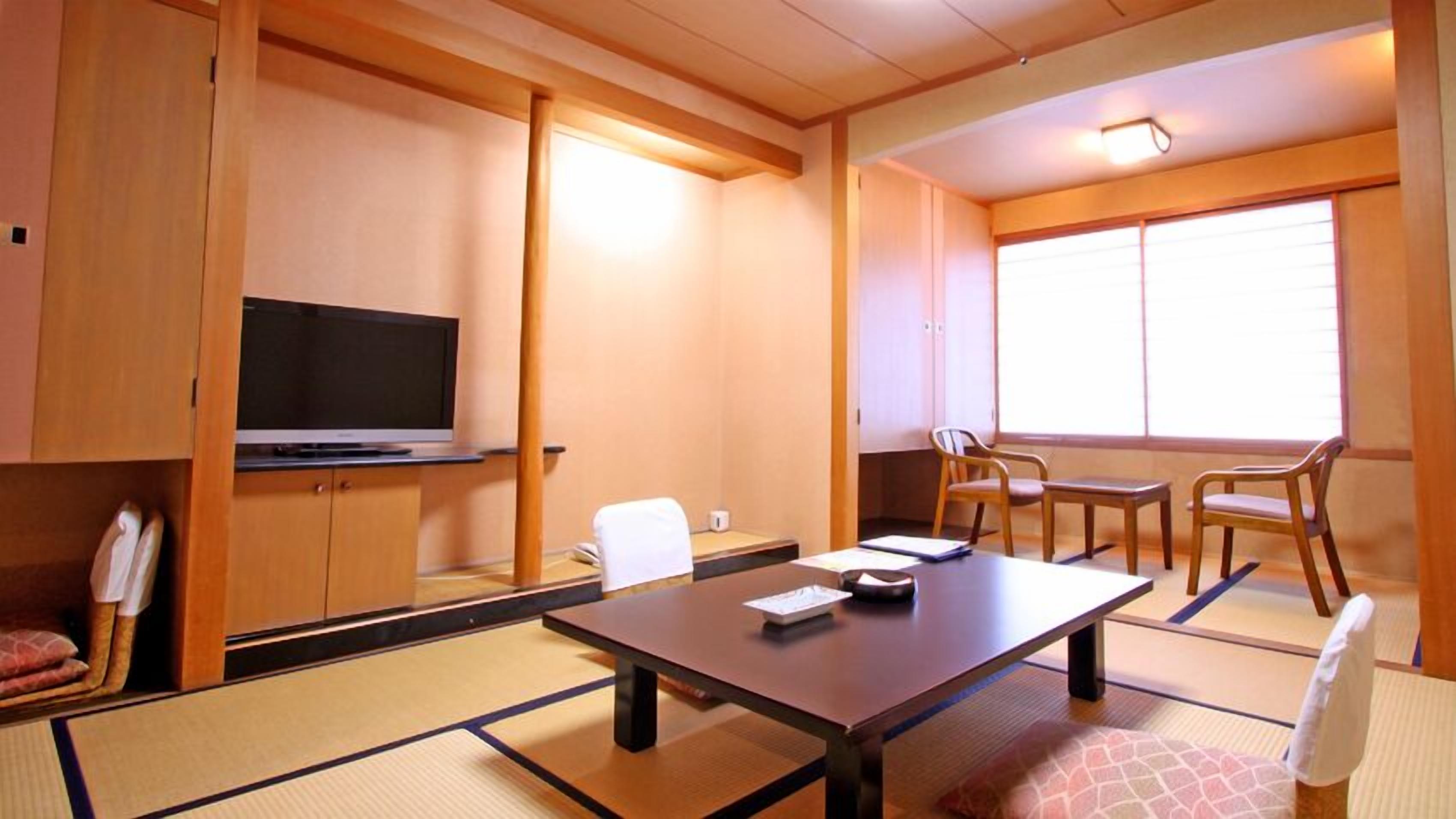Una habitación tradicional japonesa con suelo de tatami, televisor, mesa con sillas y ventana con persianas.