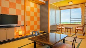 Een hotelkamer met een televisie, een eettafel, stoelen en uitzicht op zee, met een geruit behang.