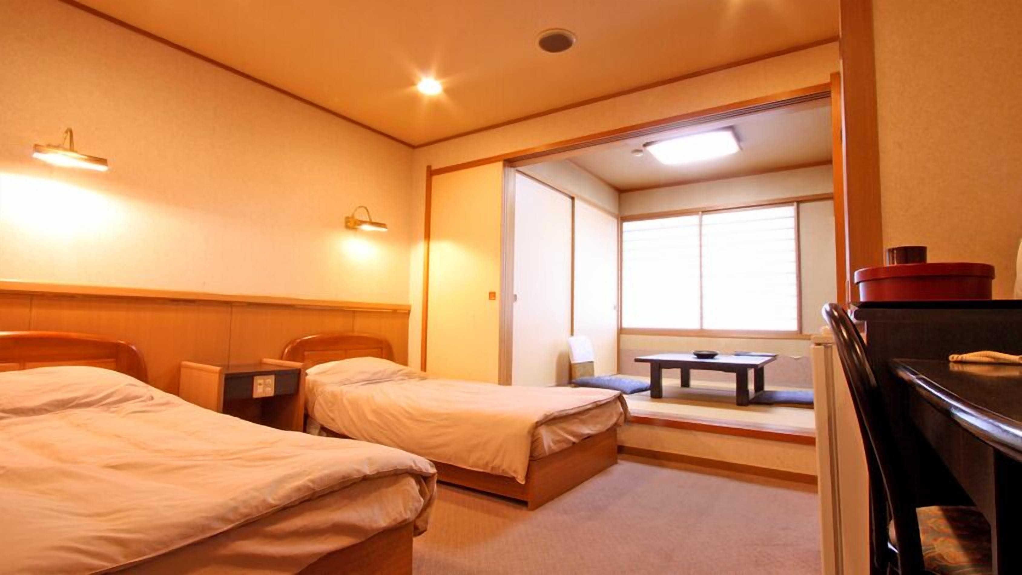 Habitación de hotel con dos camas, un escritorio, una silla, una mesa y un ventanal.