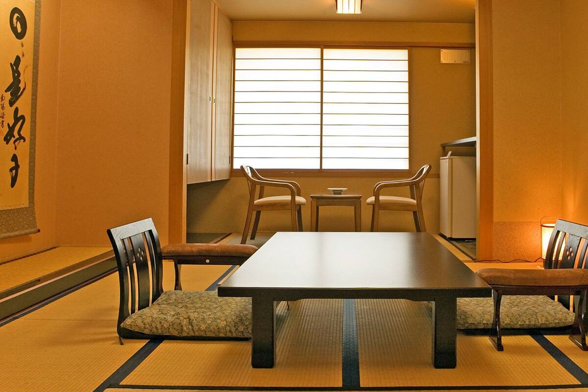 Habitació tradicional japonesa amb fons de tatami, una taula baixa i cadires de fusta.