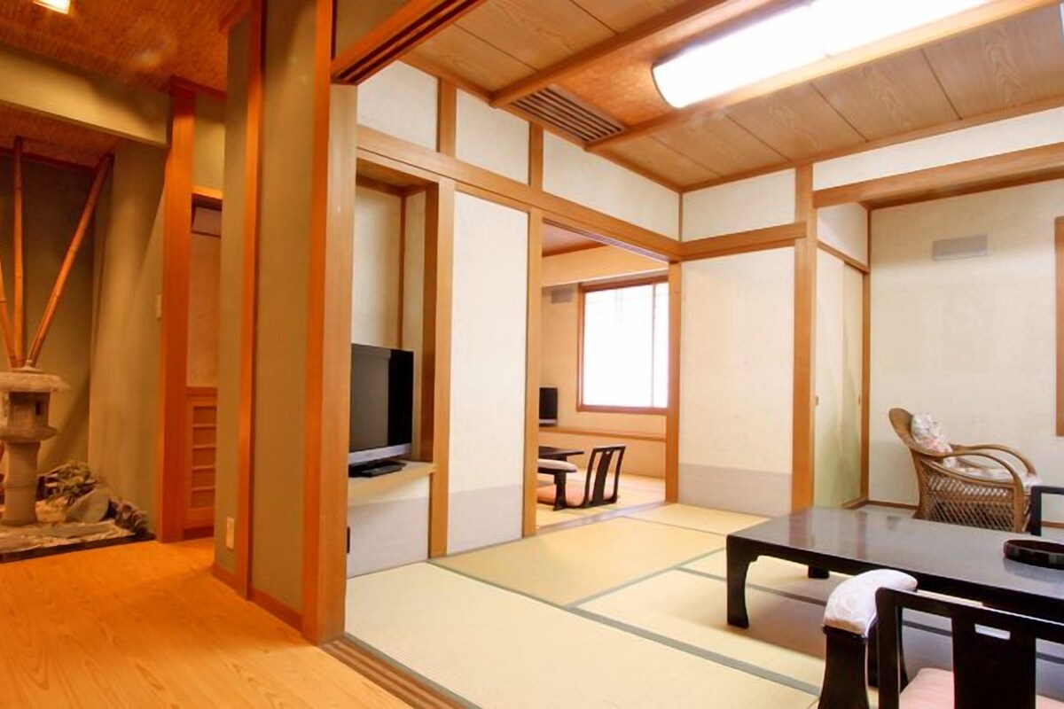 Una habitación japonesa tradicional con suelo de tatami, televisor, mesa y silla.