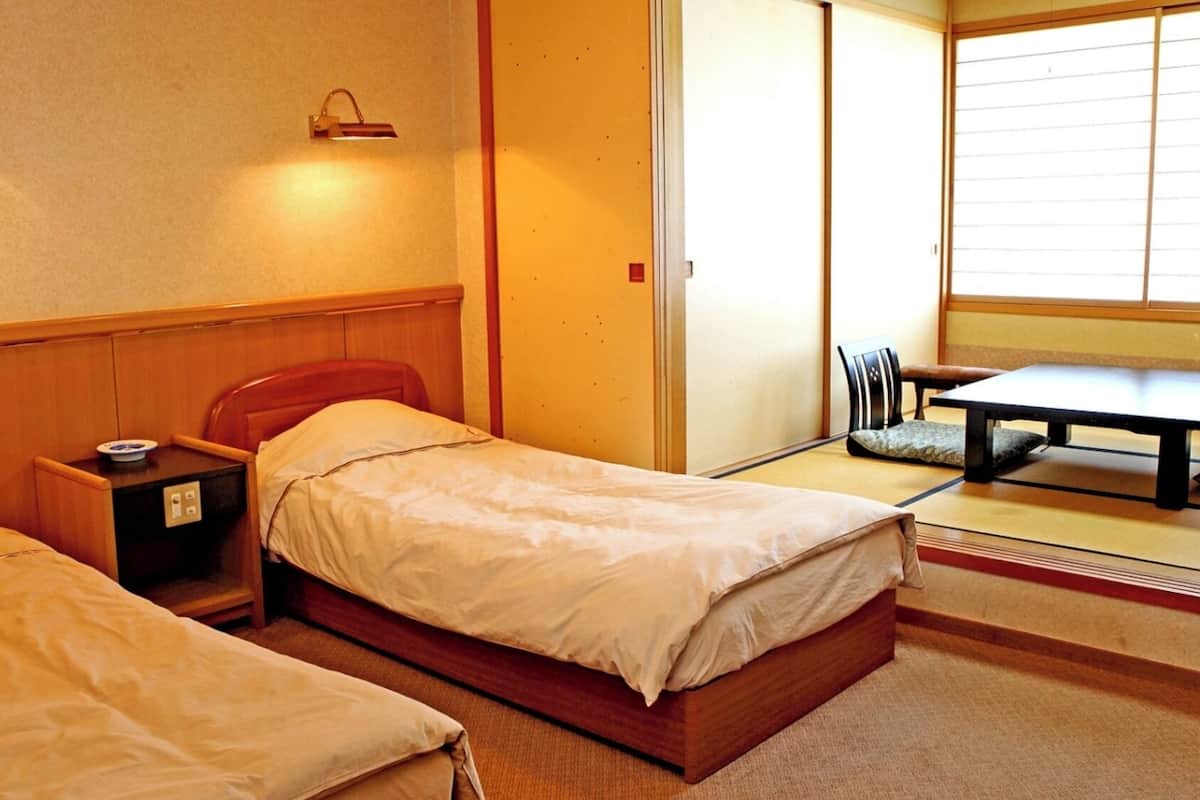 Habitació d'hotel amb dos llits individuals, una petita taula de nit amb una làmpada, una cadira, una taula i una porta corredissa.