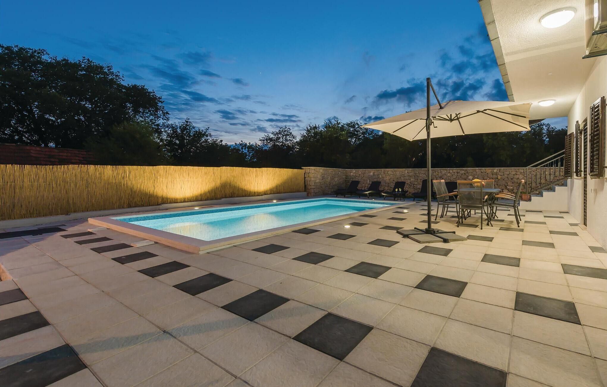 Una piscina con solárium empedrado, mobiliario exterior y una pared de piedra.