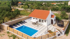 Uma villa com piscina, área de estar ao ar livre e um muro de pedra delimitando a propriedade.