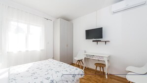 Quarto com cama, escrivaninha com cadeira, televisão e ar condicionado.