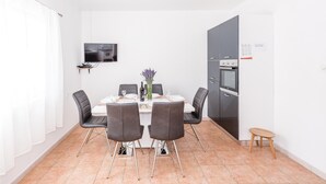 Uma sala de jantar moderna com uma mesa branca, quatro cadeiras cinzas, um pequeno vaso com flores e um forno embutido.