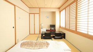 Une pièce de style japonais traditionnel, avec un sol recouvert de tatamis, un lit avec une couverture à motifs, un bureau avec un ordinateur et des portes coulissantes.