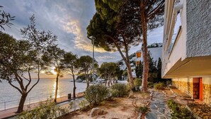 A coastal pathway with stone steps leading to a building with a red door, surrounded by trees and overlooking the sea. - Marina 4 - One Bedroom Apartment, Sleeps 4 (Roses)