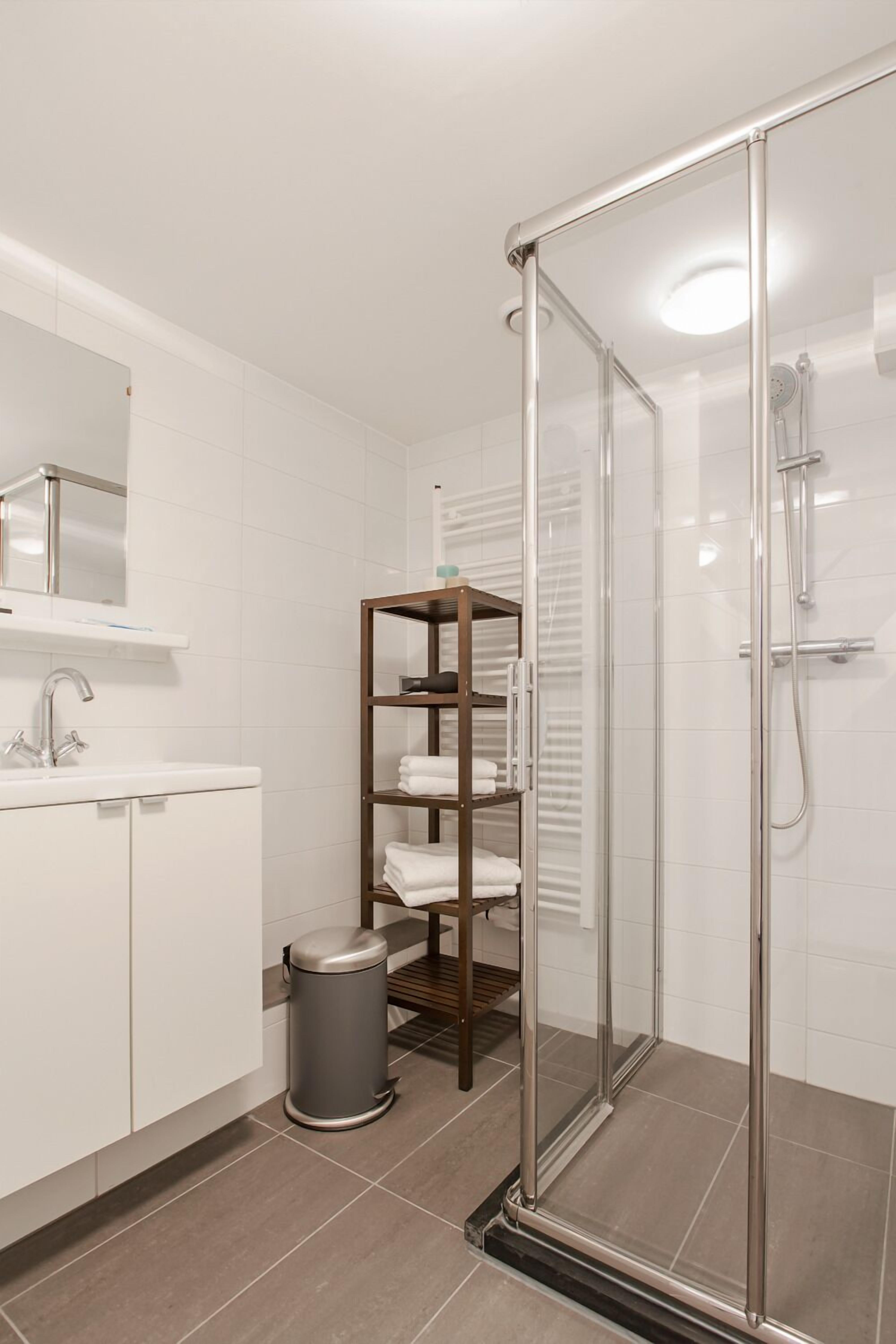A modern bathroom with a glass shower enclosure, a white sink, and a built-in shelf with towels.