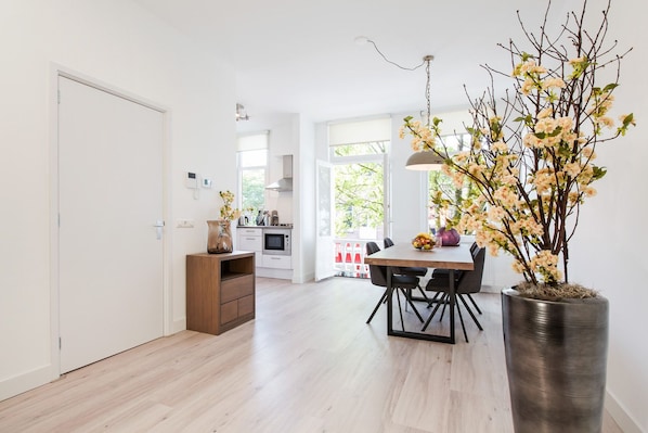 A modern kitchen with white cabinets, a wooden dining table, and a large potted plant.
