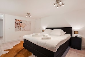 A modern bedroom with a large bed, a ceiling light fixture, and a framed picture on the wall.
