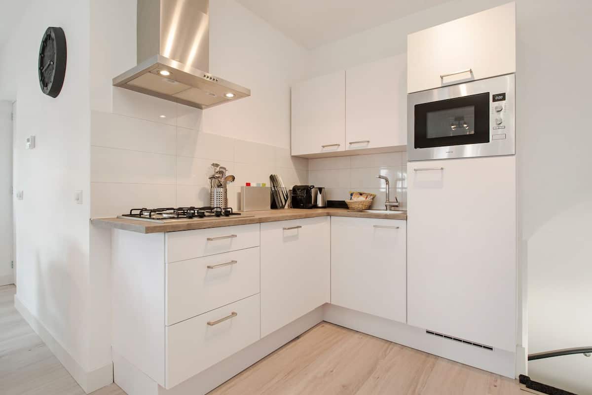 A modern kitchen with white cabinetry, a gas stove, a microwave, and a stainless steel range hood.