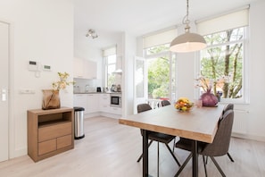 A modern kitchen with white cabinets, a wooden dining table, and a large window with a view of trees. - Windmill Apartment (Utrecht)